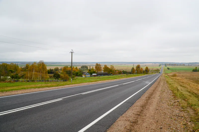 Пустое шоссе через осенние поля и деревни Беларуси